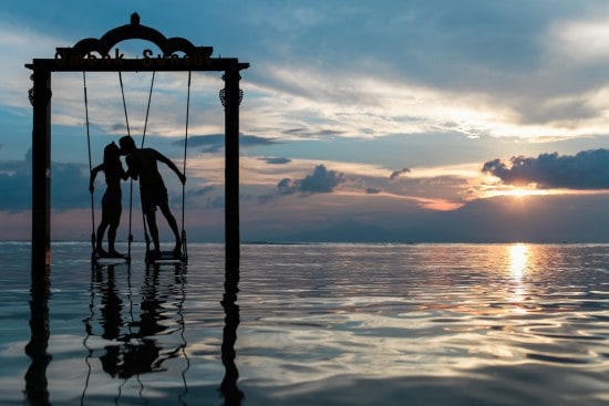 A couple enjoying a romantic sunset on a swing over calm ocean waters, perfect for beach vacations and travel lovers seeking relaxing seaside destinations.