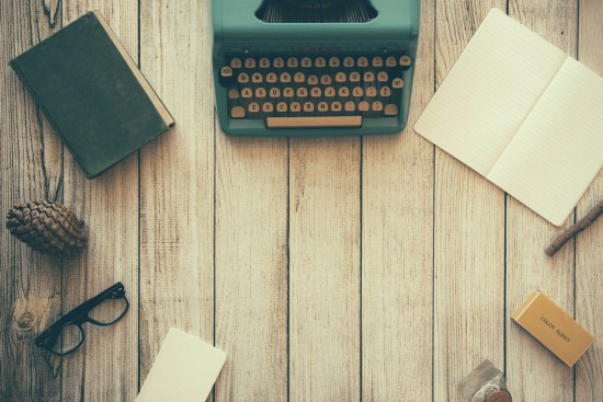 Vintage typewriter on a wooden desk with notebooks, glasses, pine cone, and other stationery, illustrating travel planning and adventure inspiration for Globe Getaways.