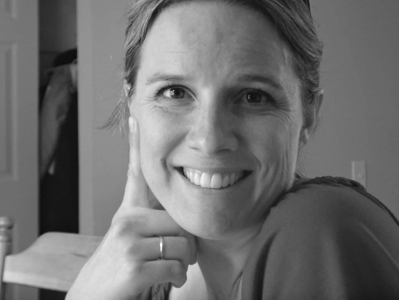 A joyful woman with short hair smiling and resting her chin on her hand, showcasing happiness and confidence, ideal for travel and vacation themes.